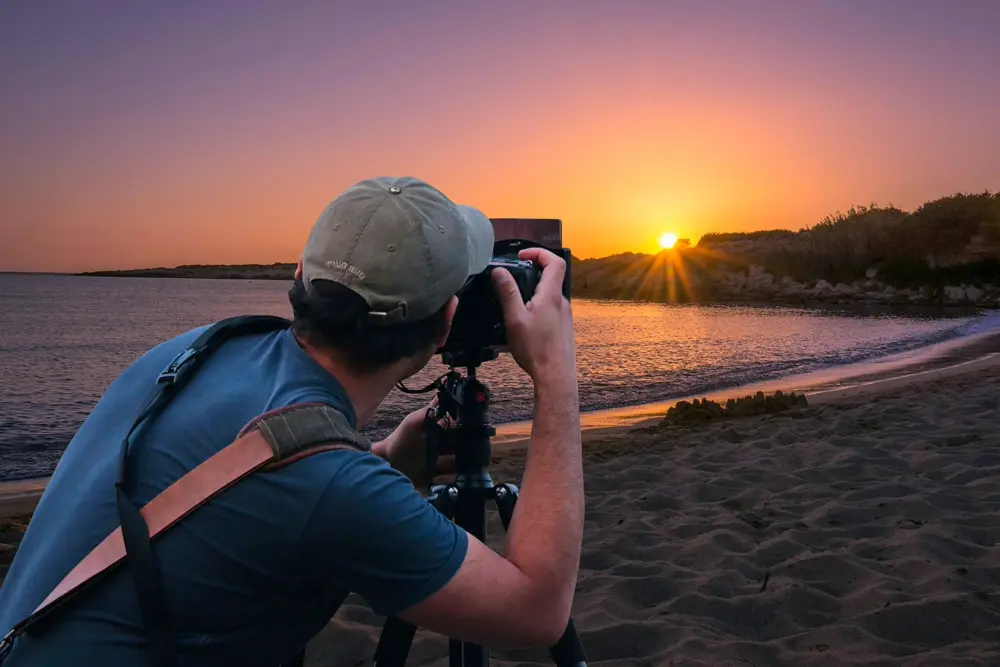 Fotógrafo con cámara en la orilla del mar al atardecer, referencia al trabajo de fotografía de sesiones en Instagram Perú